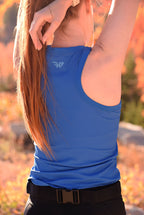 Person wearing a blue tank top with a logo, standing outdoors with a blurred natural background