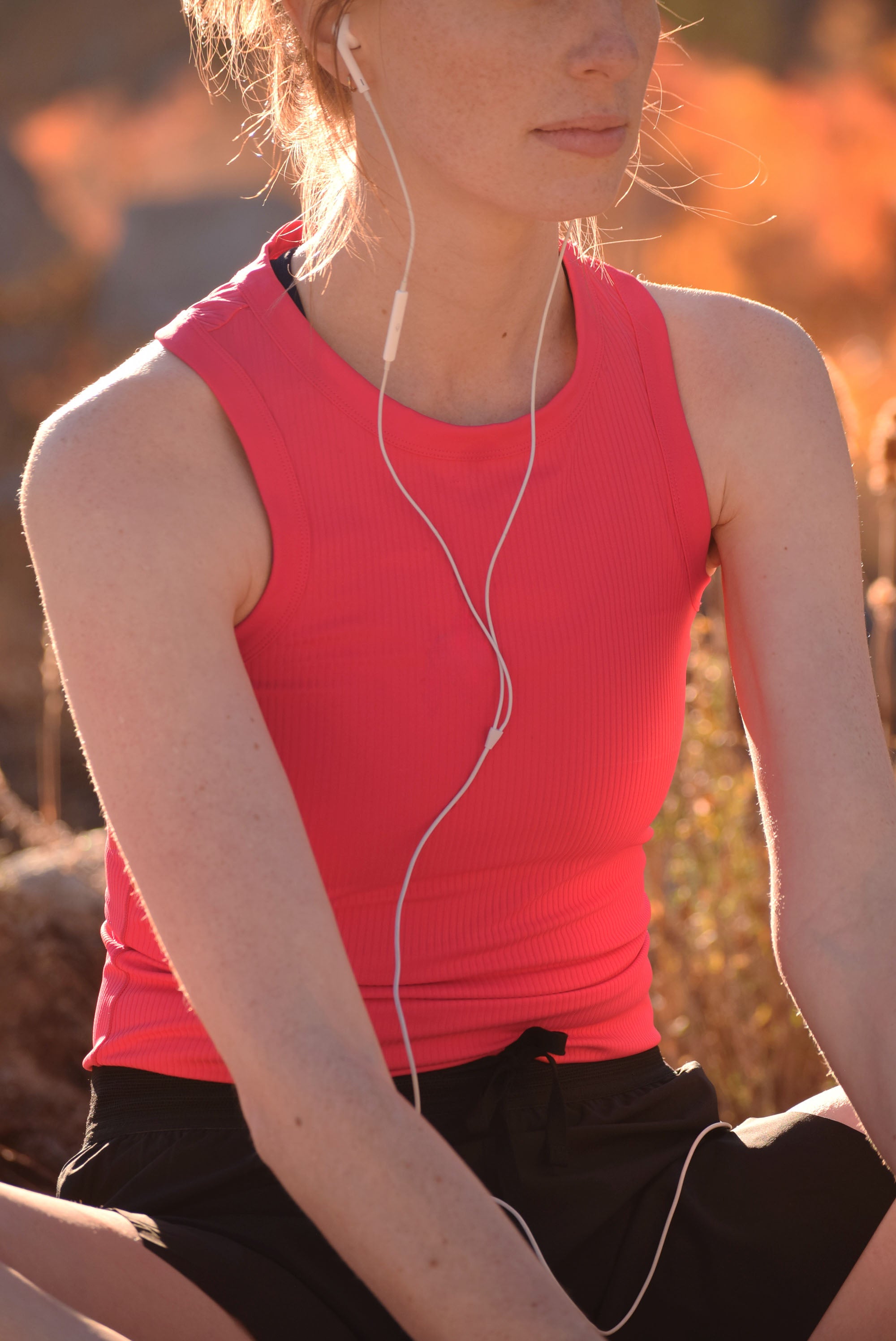 Person wearing a pink sleeveless top and black shorts with earphones, sitting outdoors.
