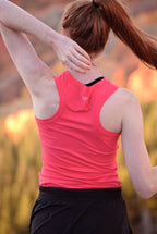 Person wearing a pink tank top with a logo, standing outdoors with blurred background