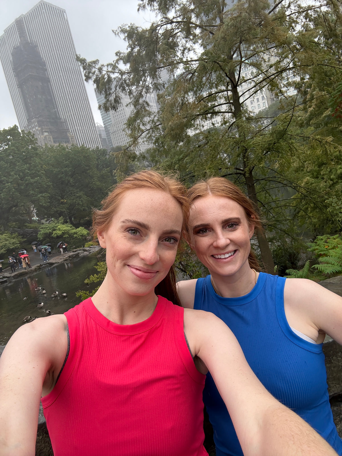 Two women taking a selfie outdoors with trees and a building in the background