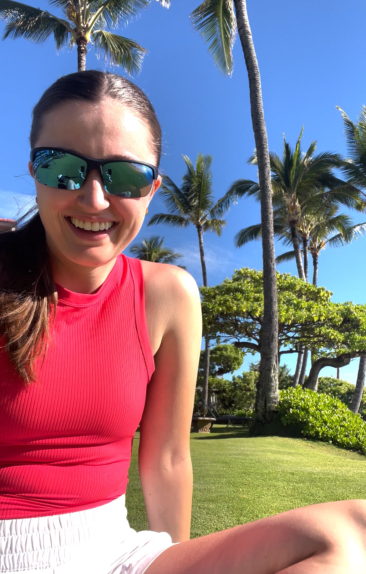 Woman wearing sunglasses and a red top with palm trees in the background