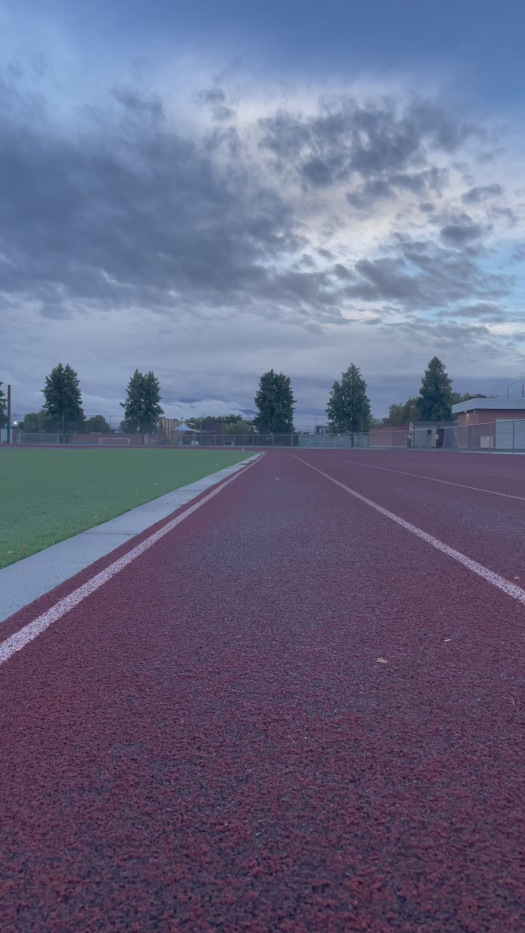 Video of a woman on a track with mountains in the background running as well as standing to show off her brightly colored tank top